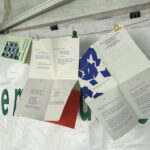 Des textes sont accrochés sur un fil devant un mur sur lequel on devine une bâche portant l'inscription "bibliothèque municipale".